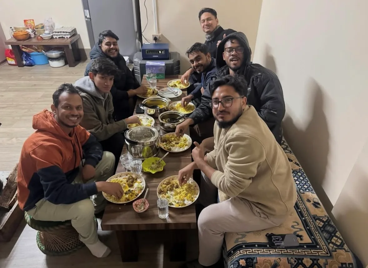 Seven travellers round a low table indoors, plates of rice and bowls of curry between them