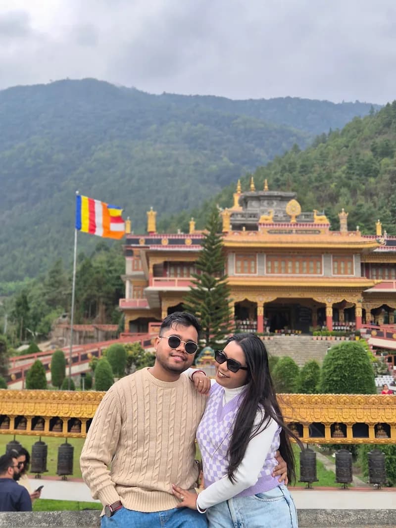 A couple in front of a gold-roofed monastery in West Arunachal, prayer wheels along the wall below