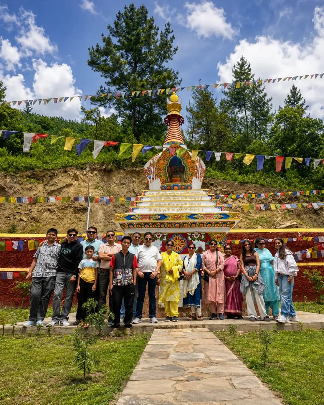 The group at a painted Buddhist chorten strung with prayer flags, pine forest above