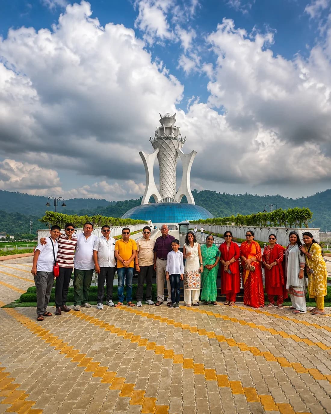 A family group of sixteen in front of a white spire and blue-domed monument in Guwahati, hills behind