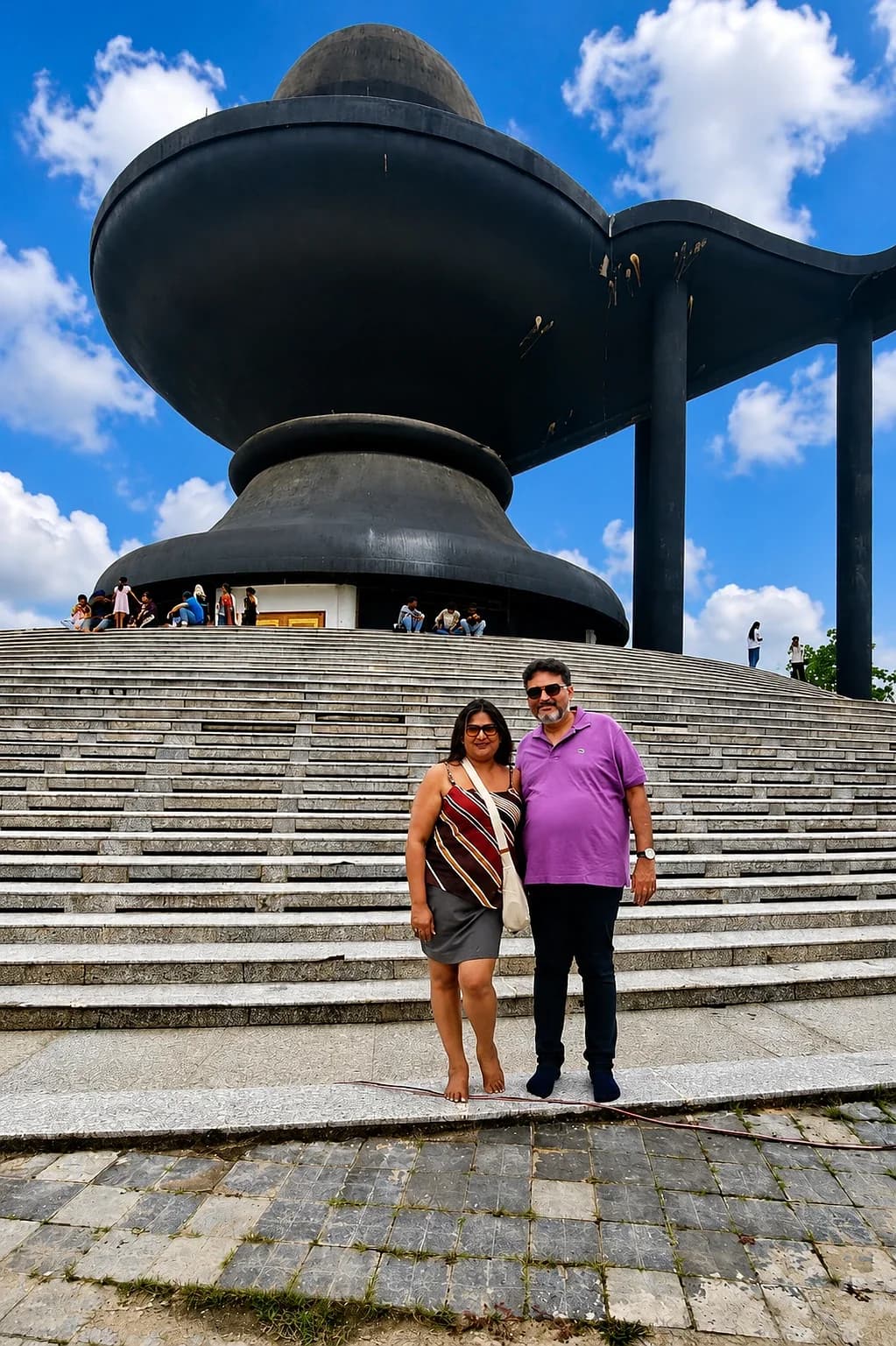 A couple on the steps below a large black domed monument under a bright sky