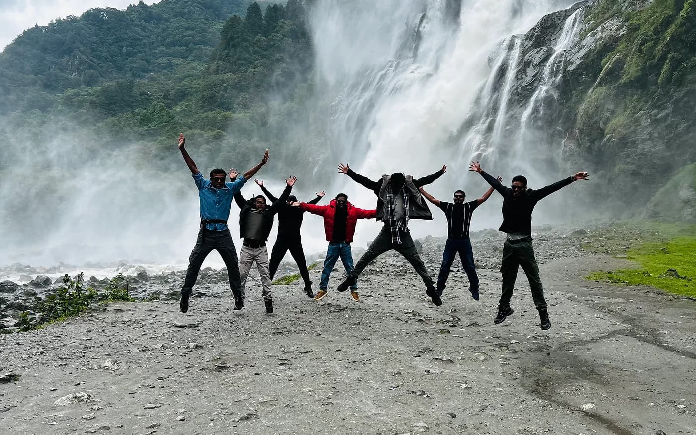 Seven travellers caught mid-jump in front of a wide, thundering waterfall