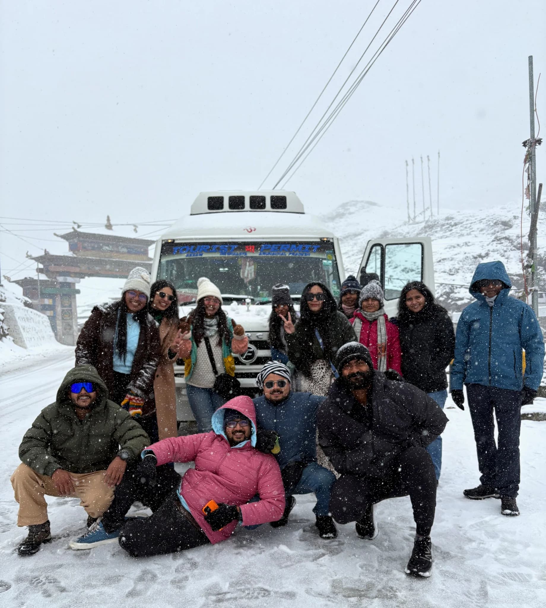 The group crowded in front of their tempo traveller on a snowbound pass, snow falling around them
