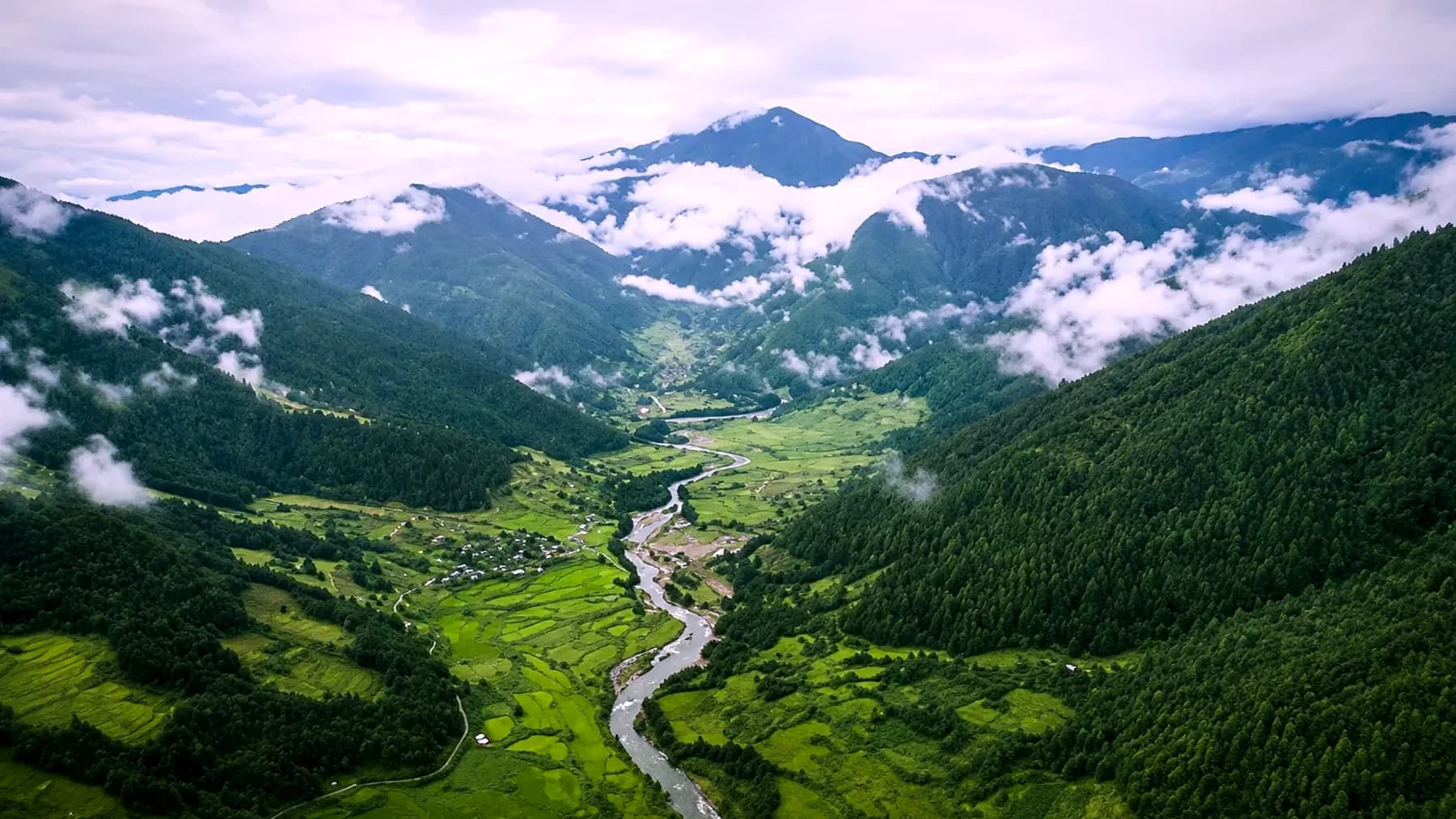 Chug Valley seen from above — a river threading terraced fields between forested slopes, with cloud sitting low against the ridges
