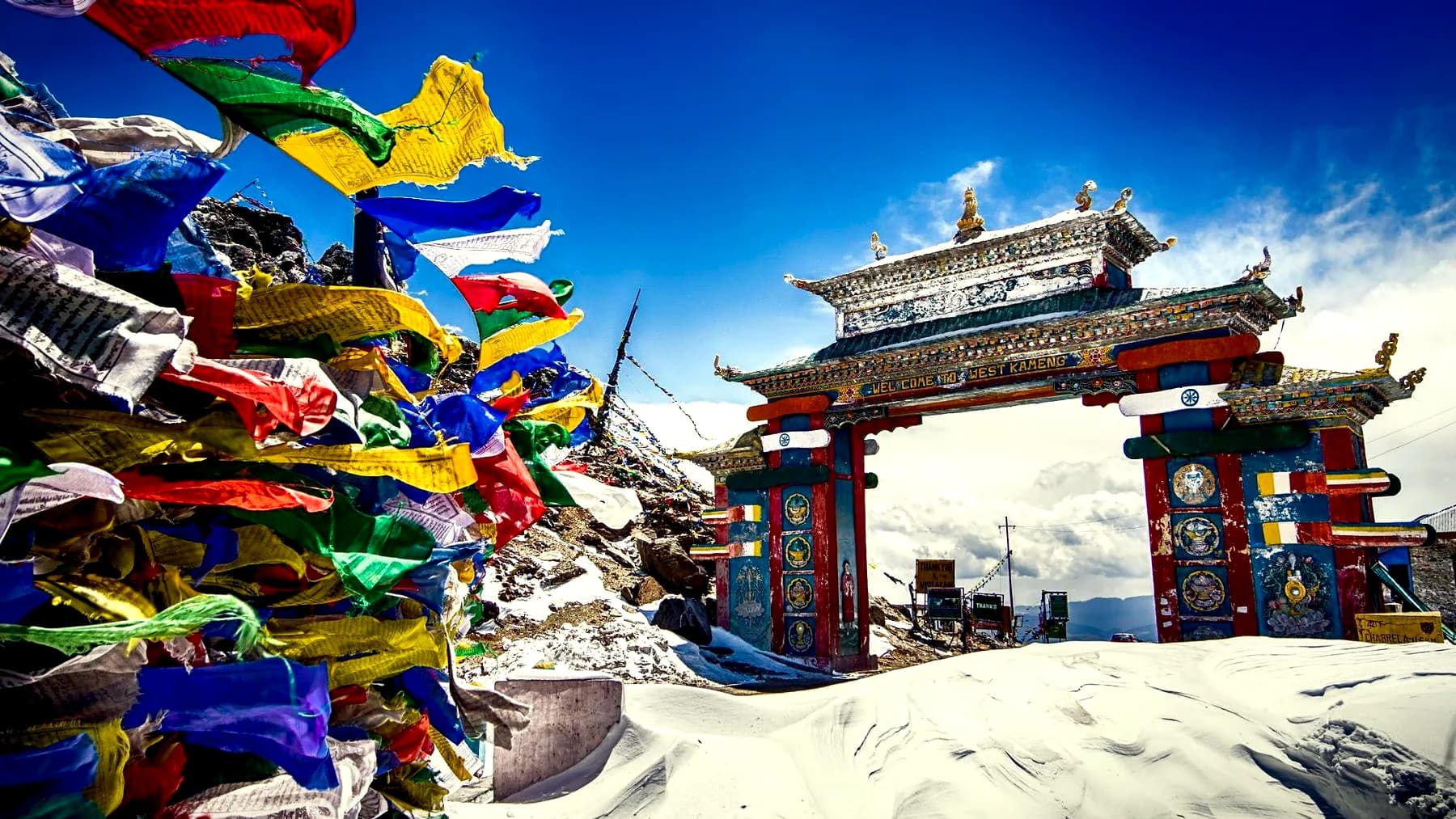 The painted gate at Sela Pass standing in deep snow, with a mass of prayer flags strung across the foreground
