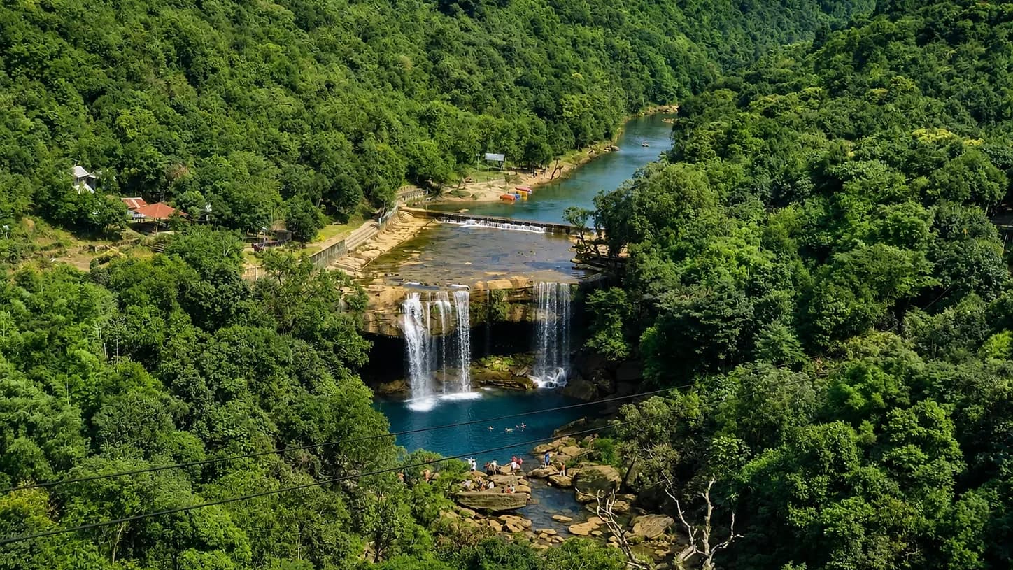 Krangsuri Falls dropping in several strands into a blue pool, forested slopes closing in on both sides