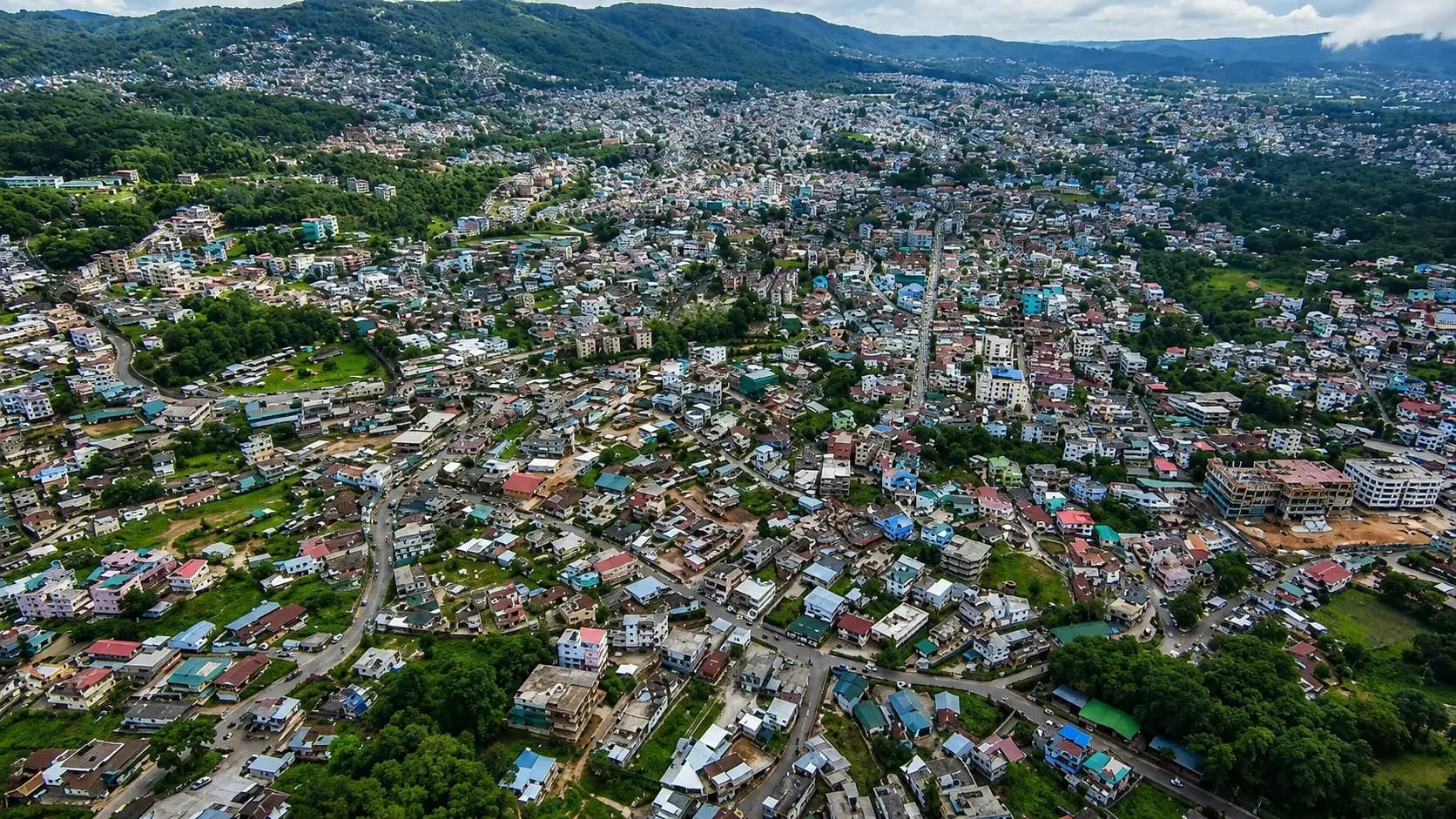 Shillong seen from the air, its coloured roofs packed across a bowl of green ridges with hills beyond
