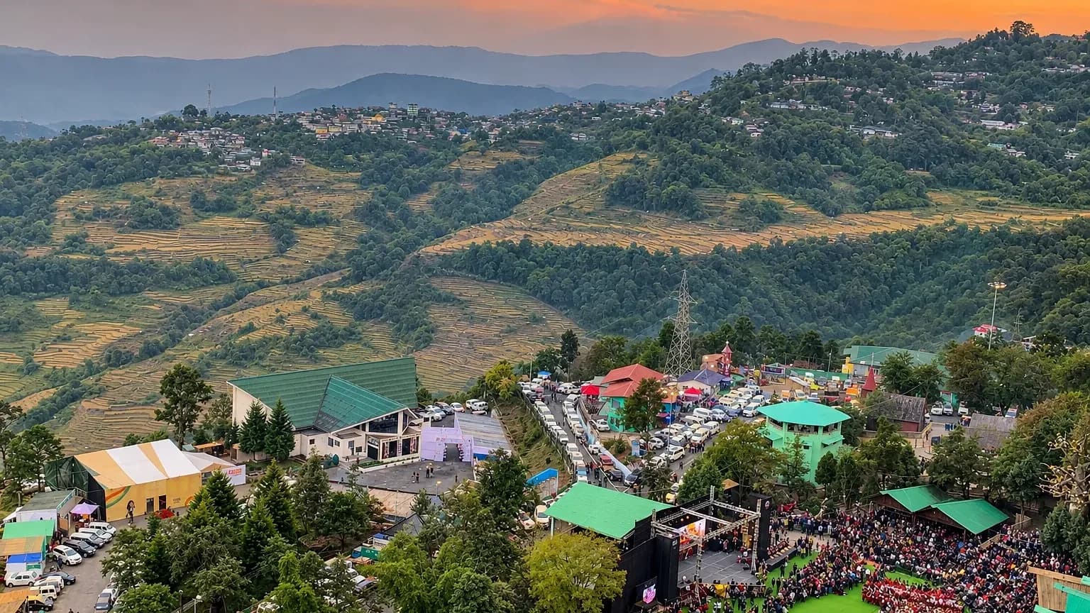 The Kisama arena at dusk with a crowd gathered before the stage, terraced hillsides catching the last light