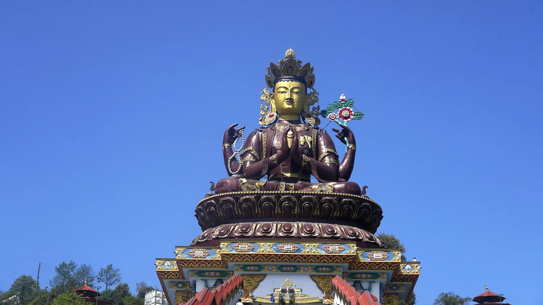 The gilded many-armed Chenrezig statue on its tiered painted base at Pelling, against a clear blue sky