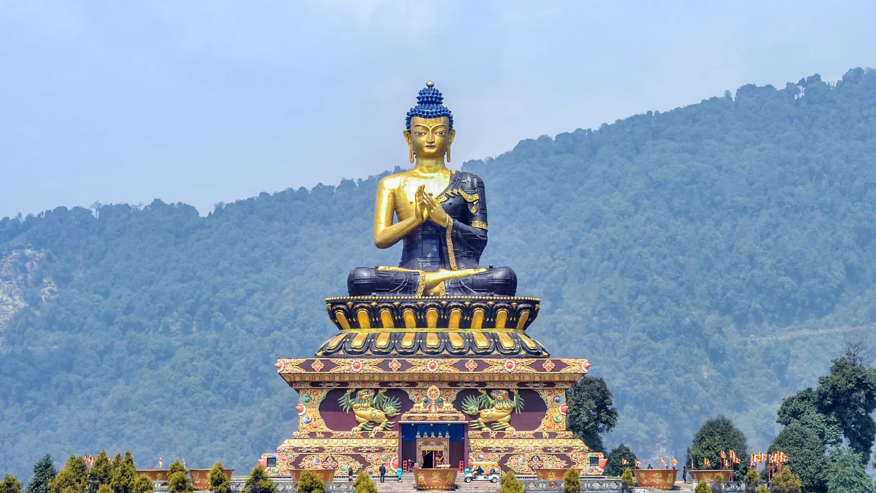 The great seated golden Buddha on its painted plinth at Buddha Park, Ravangla, forested hills behind