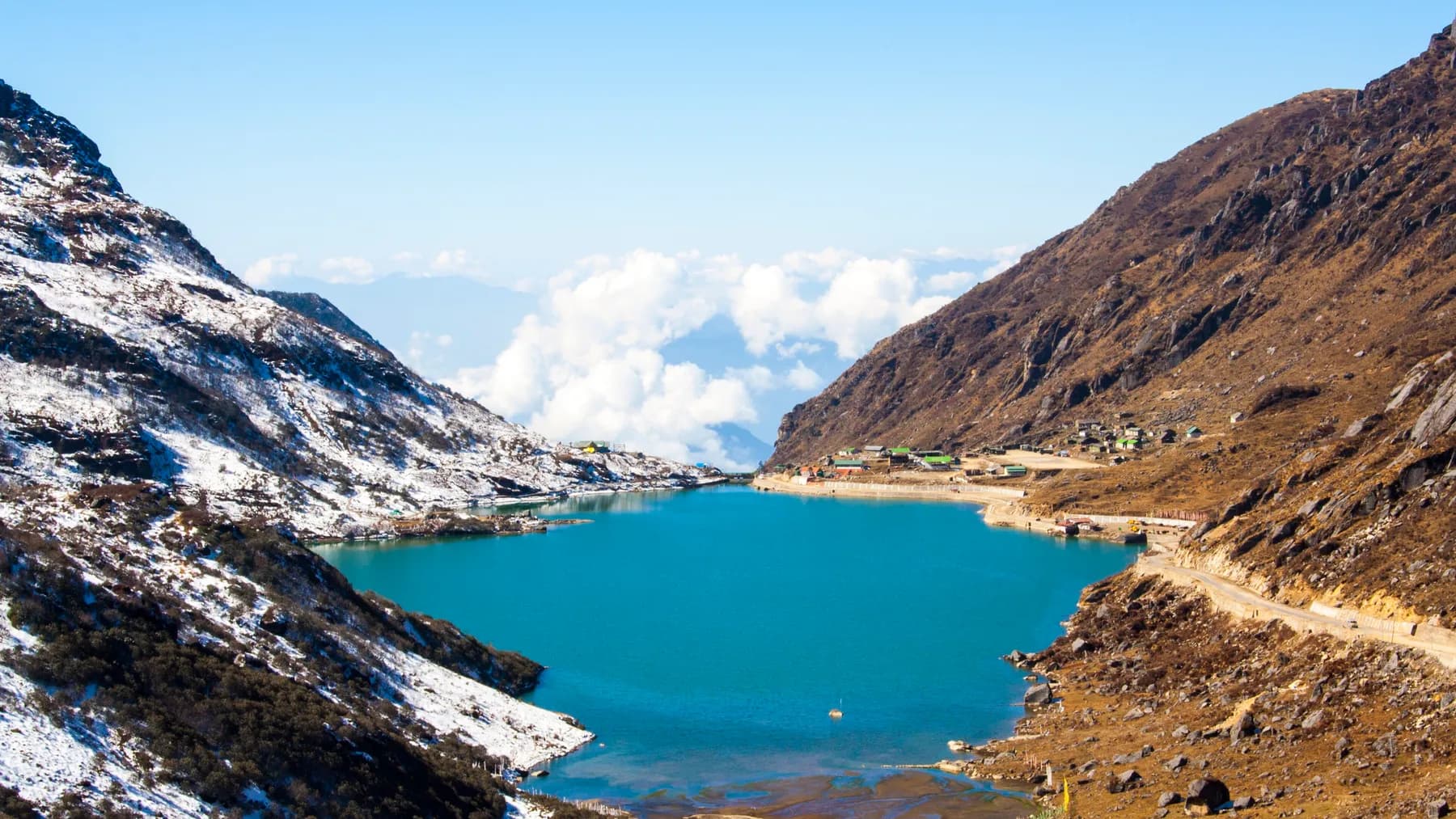 Tsomgo Lake's turquoise water between snow-streaked slopes, a bank of white cloud below the far ridge