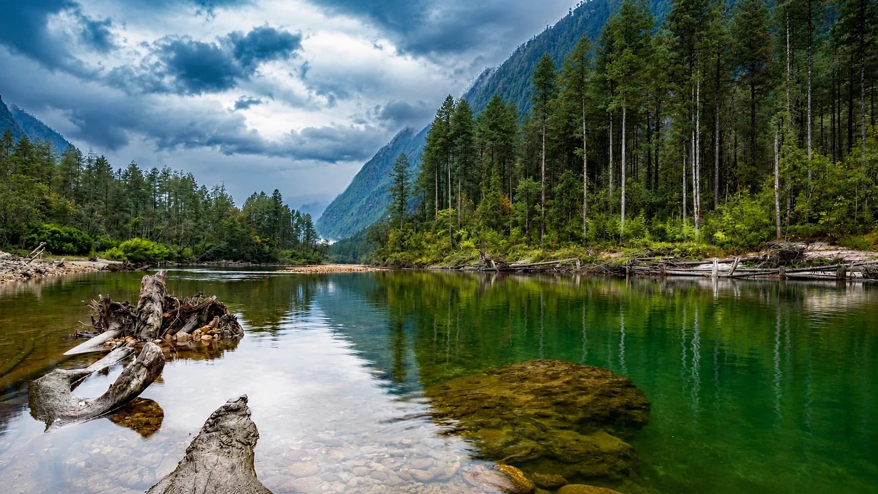 A clear green river pool below steep conifer forest in the Dibang valley, Arunachal Pradesh, under heavy cloud