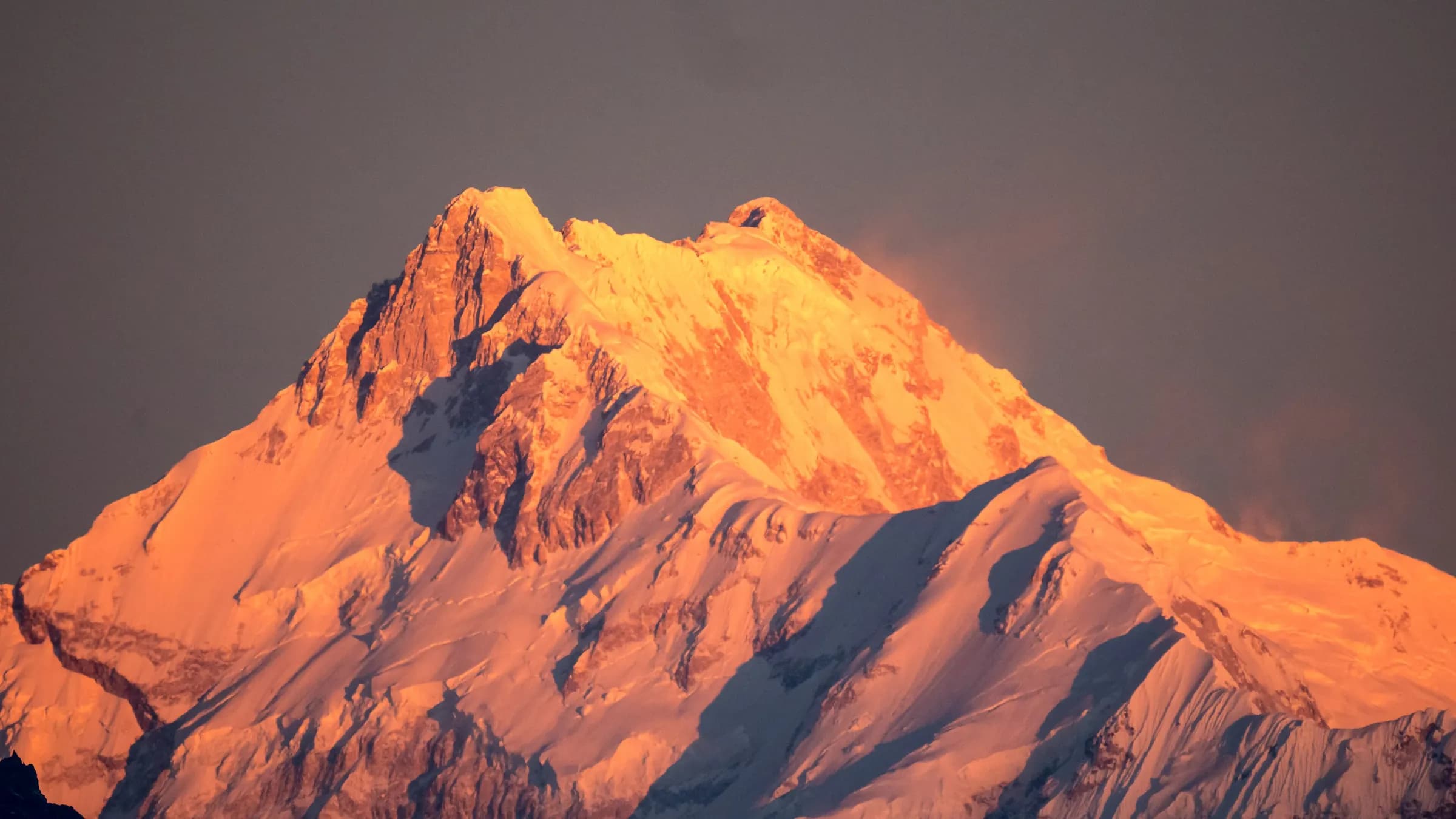 The summit of Kanchenjunga lit orange by the setting sun above a darkening sky, seen from Gangtok, Sikkim