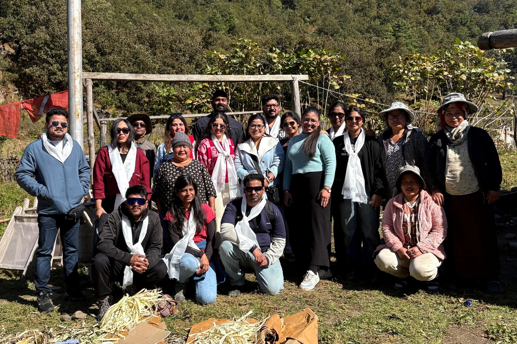 A batch and their hosts in a hillside clearing, everyone wearing the white khada scarves they were welcomed with